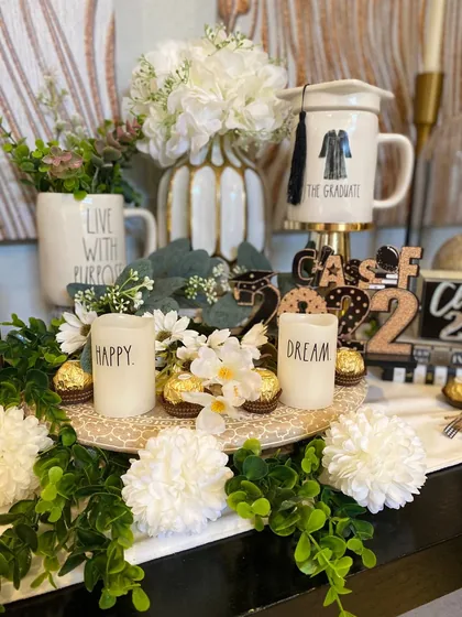 Graduation dessert table with a cap and gown mug, candles and white florals